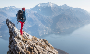 Eine Wanderin steht am Gipfel an einer Klippe und schaut in die Ferne.
