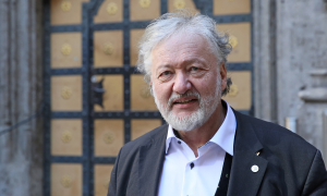 Reinhard Bauer, graue Haare und Bart, vor einer alten Tür mit Sacko