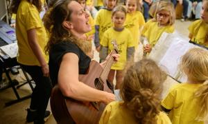 Madlen Schuh spielt auf der Gitarre, drum herum Kinder mit gelben T-Shirts