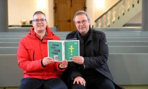 Der liturgische Lektor Elmar Glöckner und Pfarrer Andreas Funk in der Sankt Georgskirche in Möttingen halten gemeinsam das Buch hoch"Einfach Bibel".