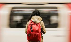 eine Frau mit Rucksack vor einem vorbeifahrenden Zug