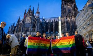 Bunte Fahne mit "Segen für alle" drauf vor einer Kirche